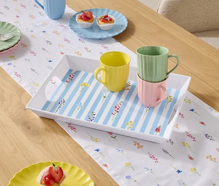 Table à manger avec vaisselle et tasses sur une nappe à fleurs.