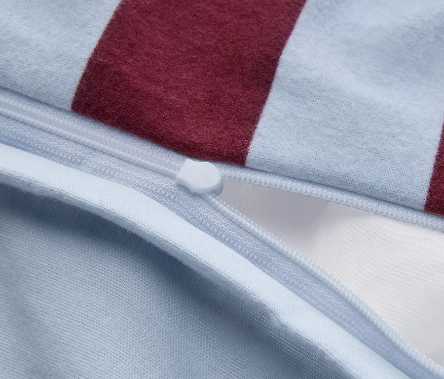 Gros plan sur un tissu rayé bleu clair et bordeaux avec une fermeture éclair bleu clair partiellement ouverte, révélant un tissu blanc à l'intérieur.