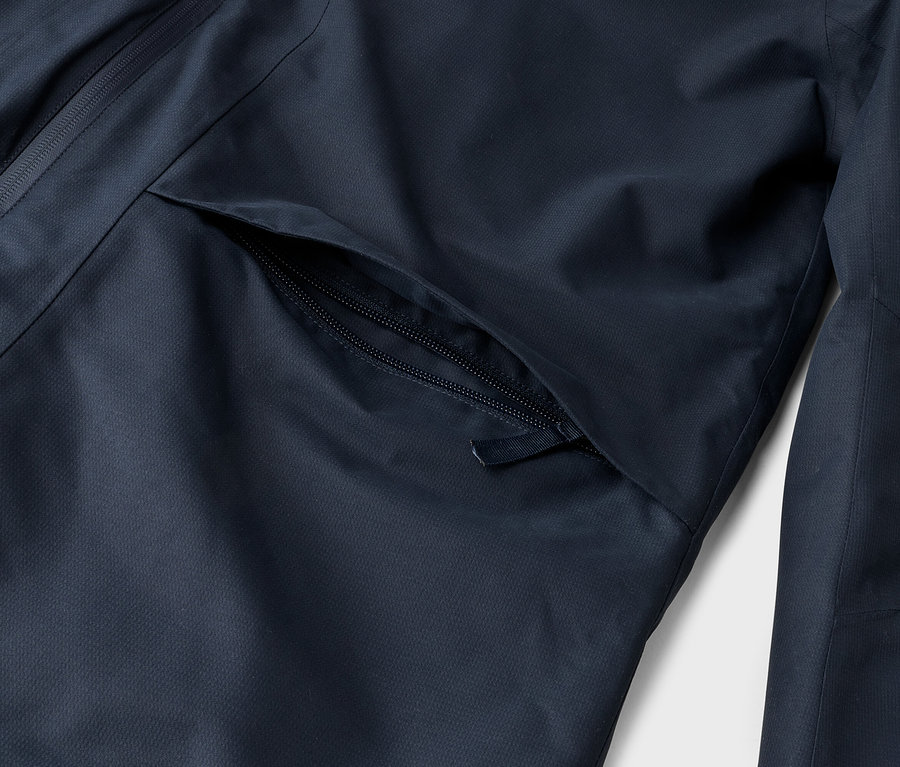 Gros plan d'une veste bleu foncé, montrant une poche zippée partiellement ouverte sur le devant et une fermeture éclair verticale sur le côté gauche.