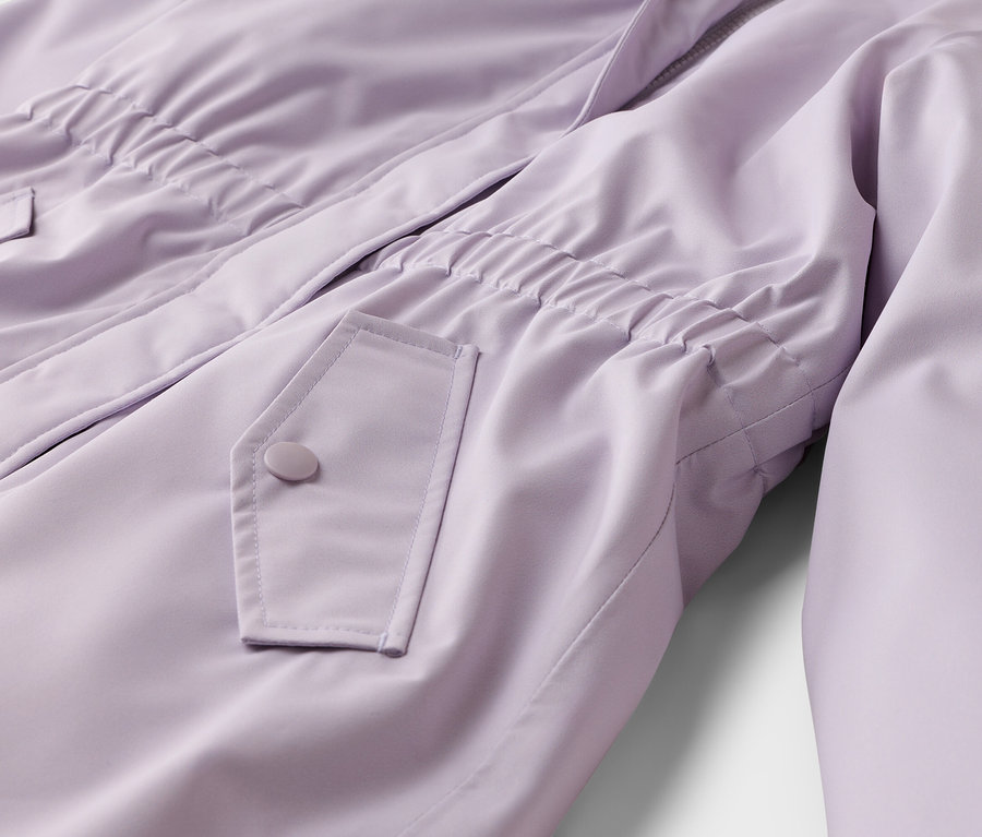 Gros plan d'une veste lilas avec une taille élastiquée, une poche à rabat boutonnée et une fermeture éclair partiellement visible.