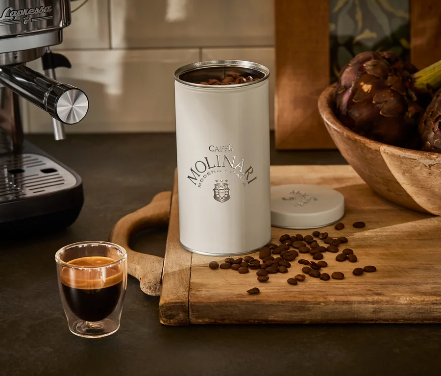 Machine à expresso à côté d'une tasse et d'une boîte de Caffe Molinari sur une planche en bois.