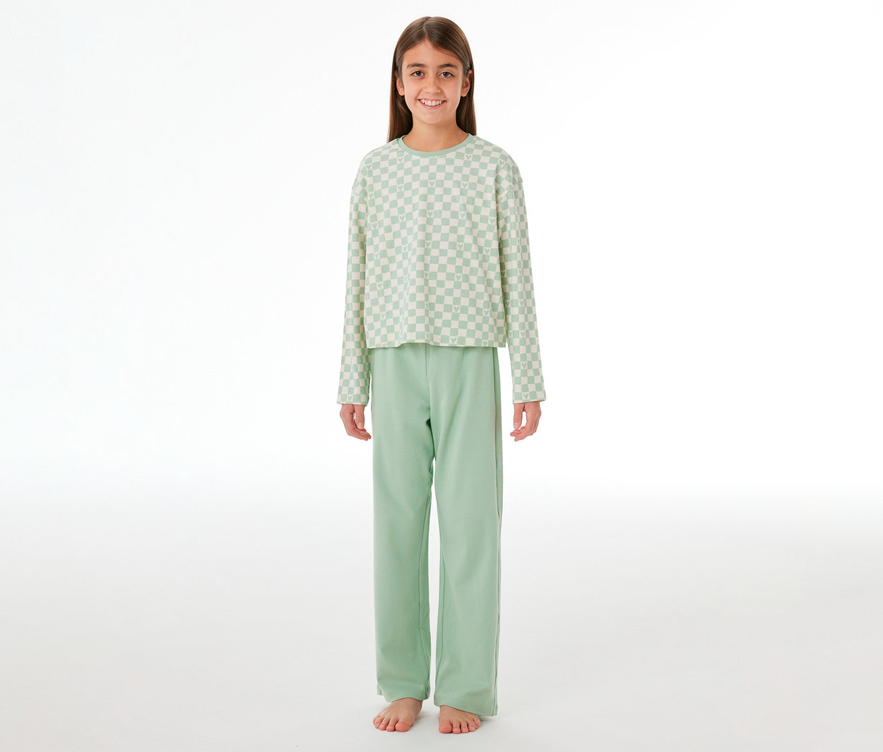 Jeune fille souriante portant un pyjama Interlock SCHIESSER pour enfant. Le haut est à carreaux vert clair et blanc, le pantalon est vert clair uni.