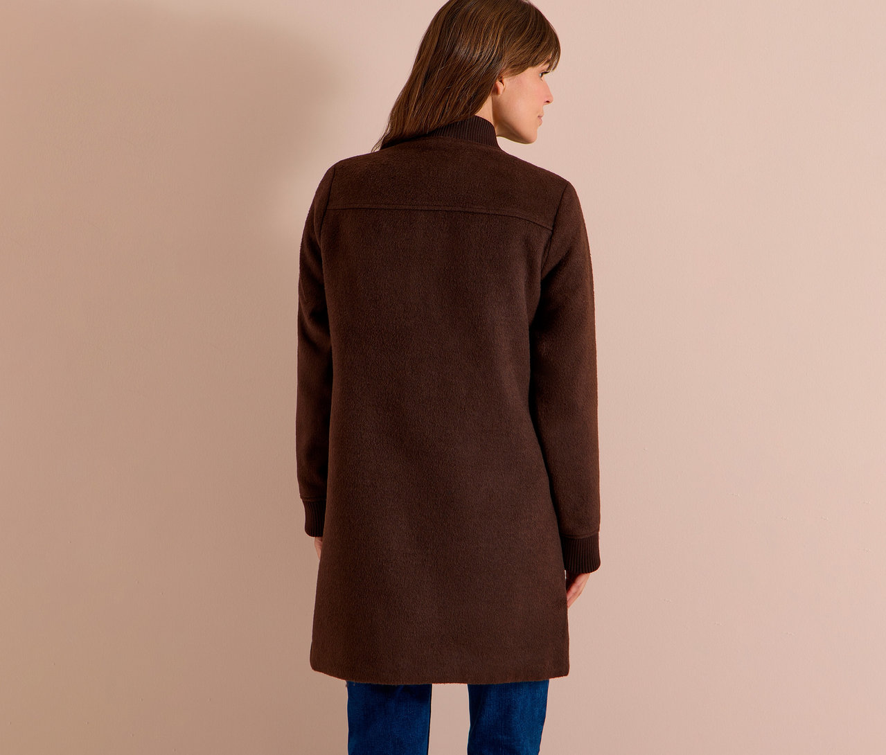 Femme vue de dos, légèrement tournée, portant un blouson CECIL marron foncé sur un jean bleu.