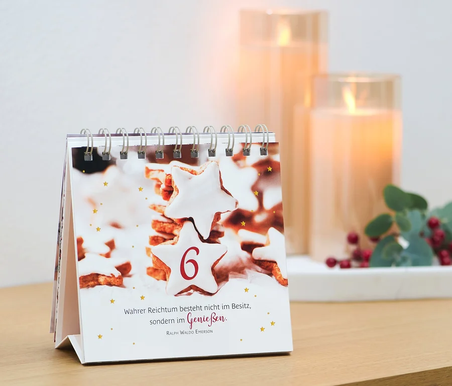 Un calendrier de table avec une image de biscuits et le chiffre 6, à côté de bougies et d'une décoration. Livre/présentoir : « Merveilles de l’Avent »