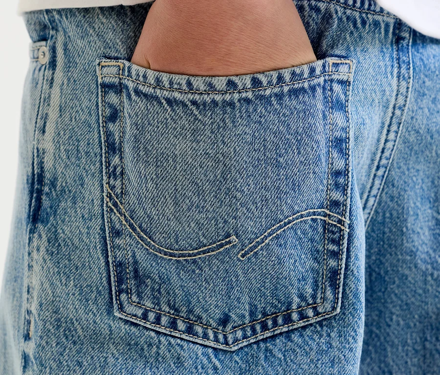 Gros plan d'une main dans la poche arrière d'un jean bleu clair avec des coutures visibles.