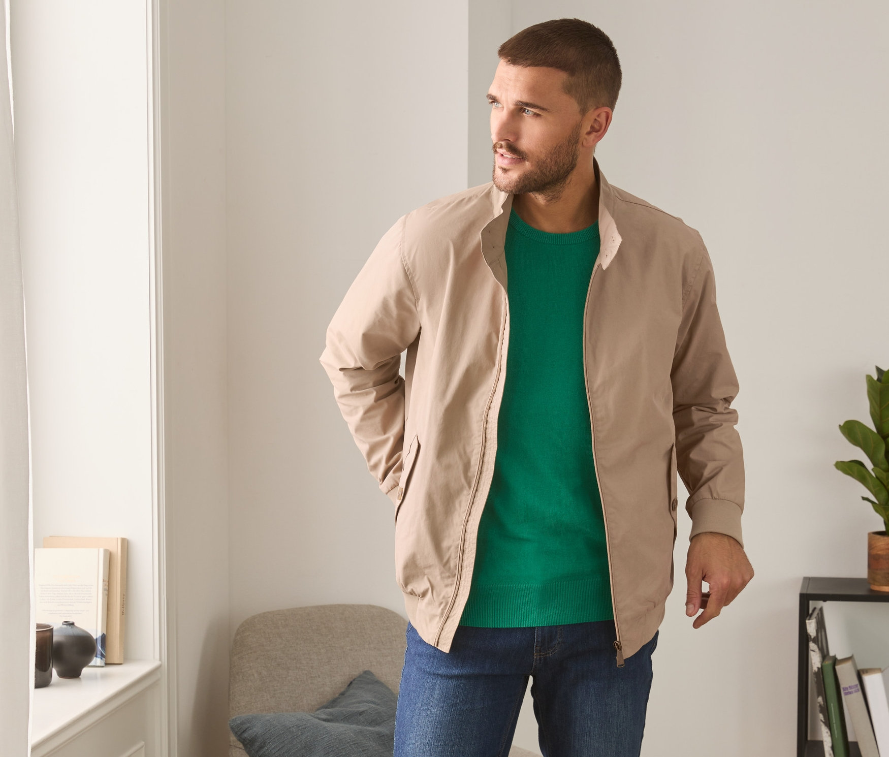 Un homme portant un blouson beige, un t-shirt vert et un jean.