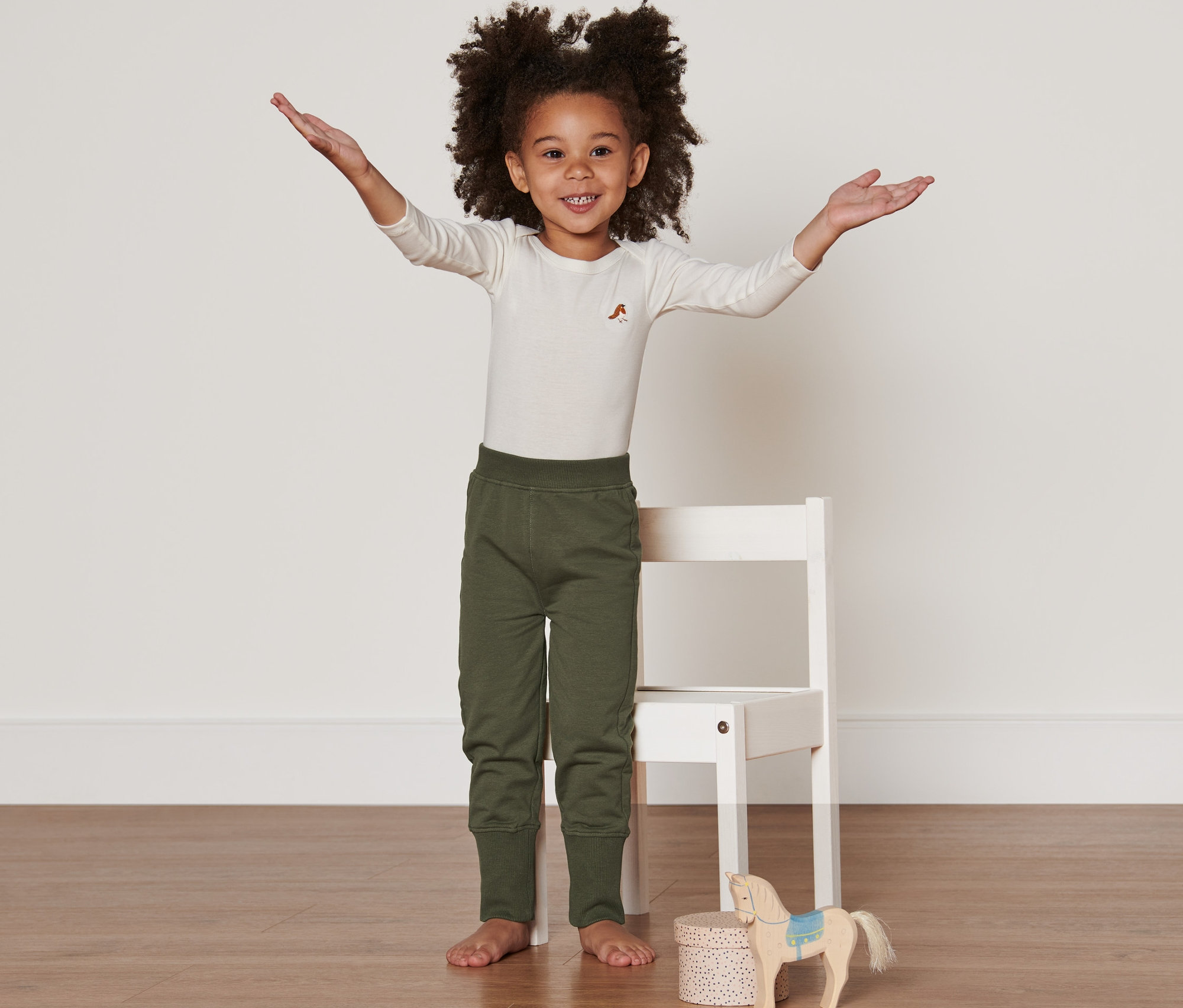 Une fille se tient debout, les bras écartés, portant 2 pantalons de survêtement.