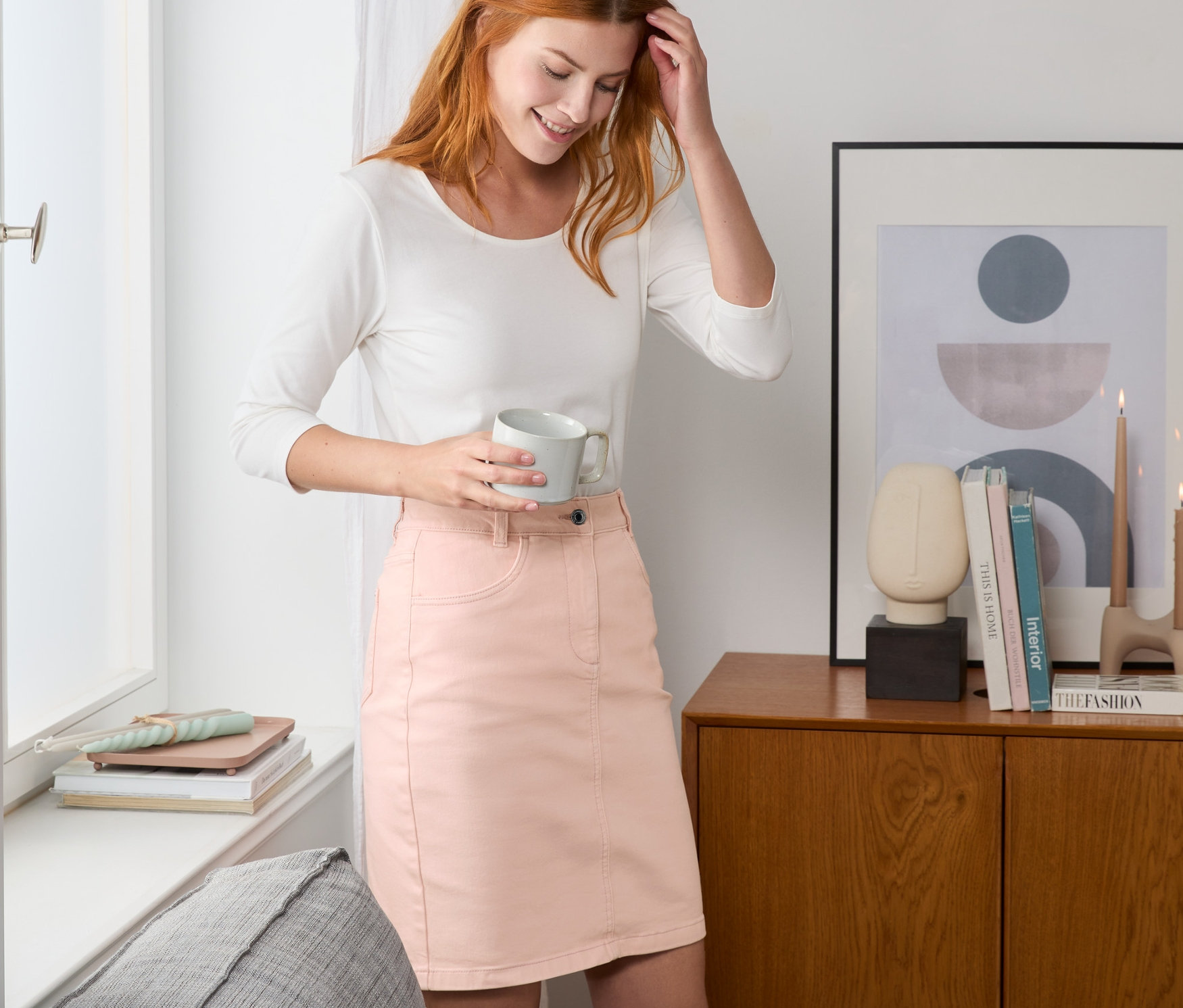 Femme tenant une tasse et portant une jupe en jean rose.