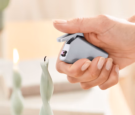 Une femme allume une bougie avec un briquet électrique.