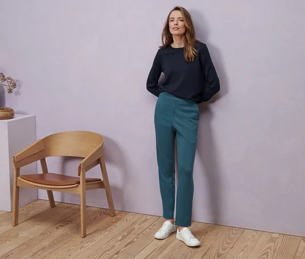 Une femme porte des baskets en cuir, un pullover en maille fine de mérinos bleu foncé et un pantalon de jogging.