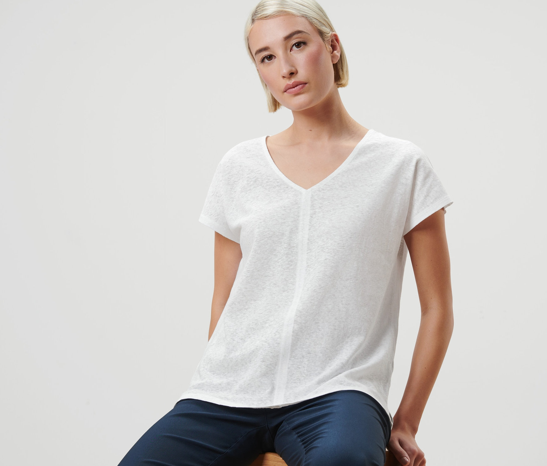 Une femme est assise sur un tabouret et porte une blouse en lin blanc crème.