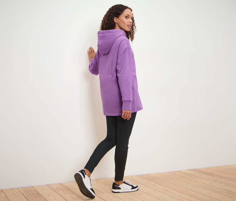 Femme marchant, portant un sweatshirt long à capuche, un legging noir et des baskets.