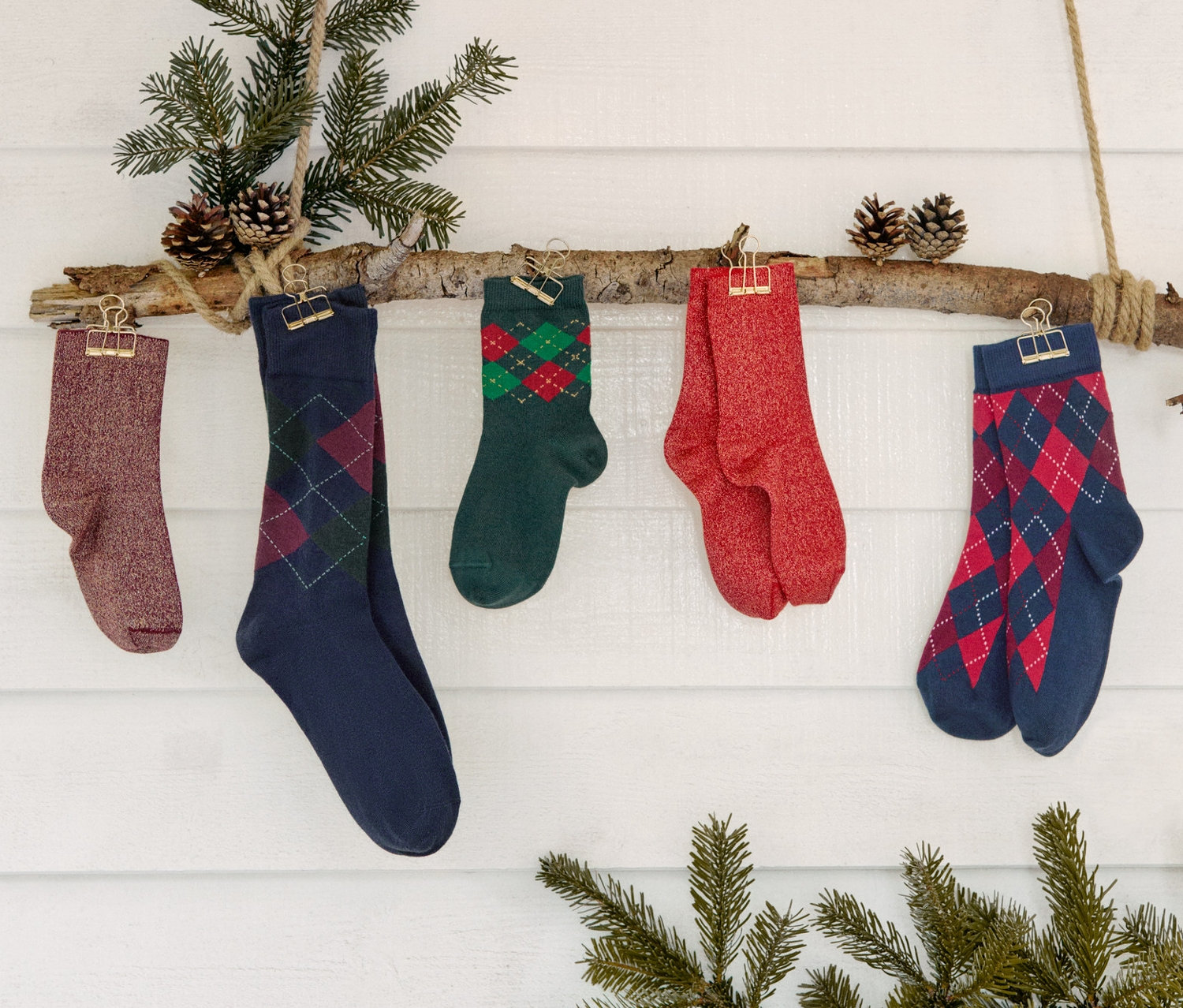 Cinq paires de chaussettes et trois paires de chaussettes scintillantes pour enfants accrochées à une branche décorée de sapin et de pommes de pin.