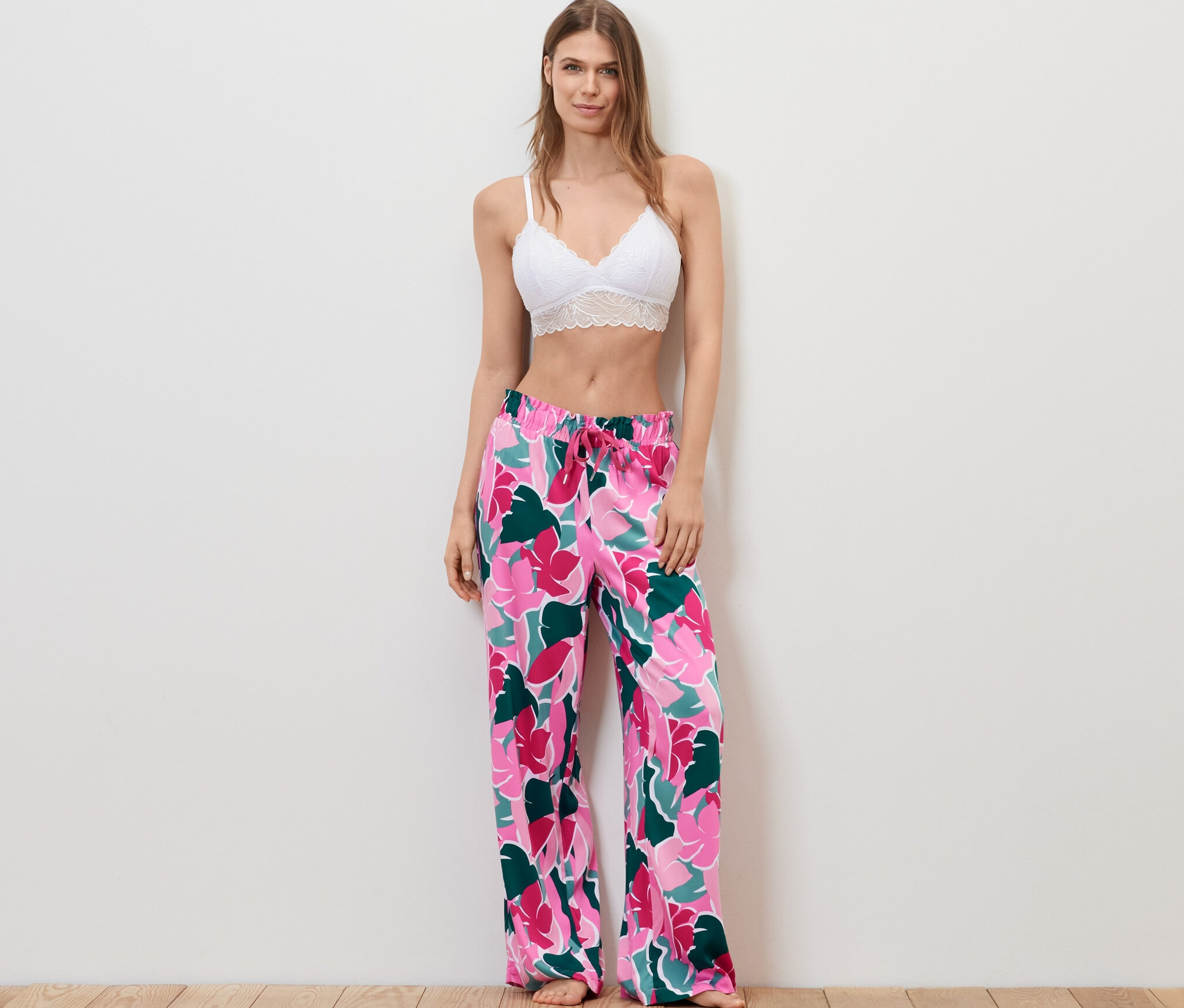 Une femme debout portant un soutien-gorge en dentelle blanche et un pantalon relax à motif floral.