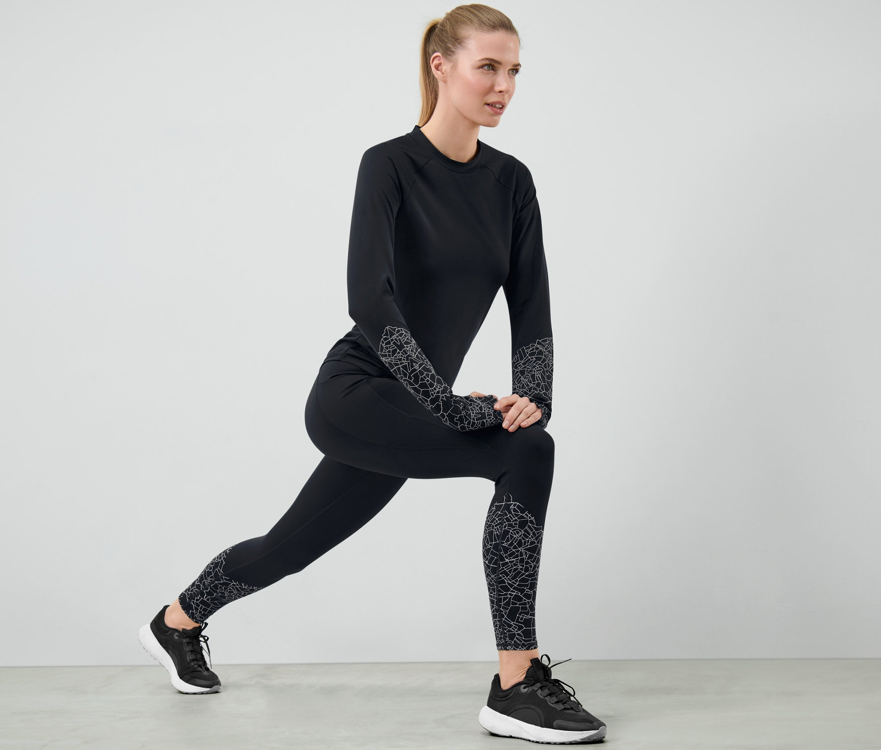 Femme en legging de sport noir et haut de sport noir faisant des étirements.