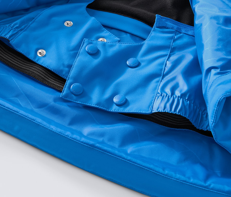 Détail d'une veste de ski bleue high-tech avec boutons et ourlet noir.