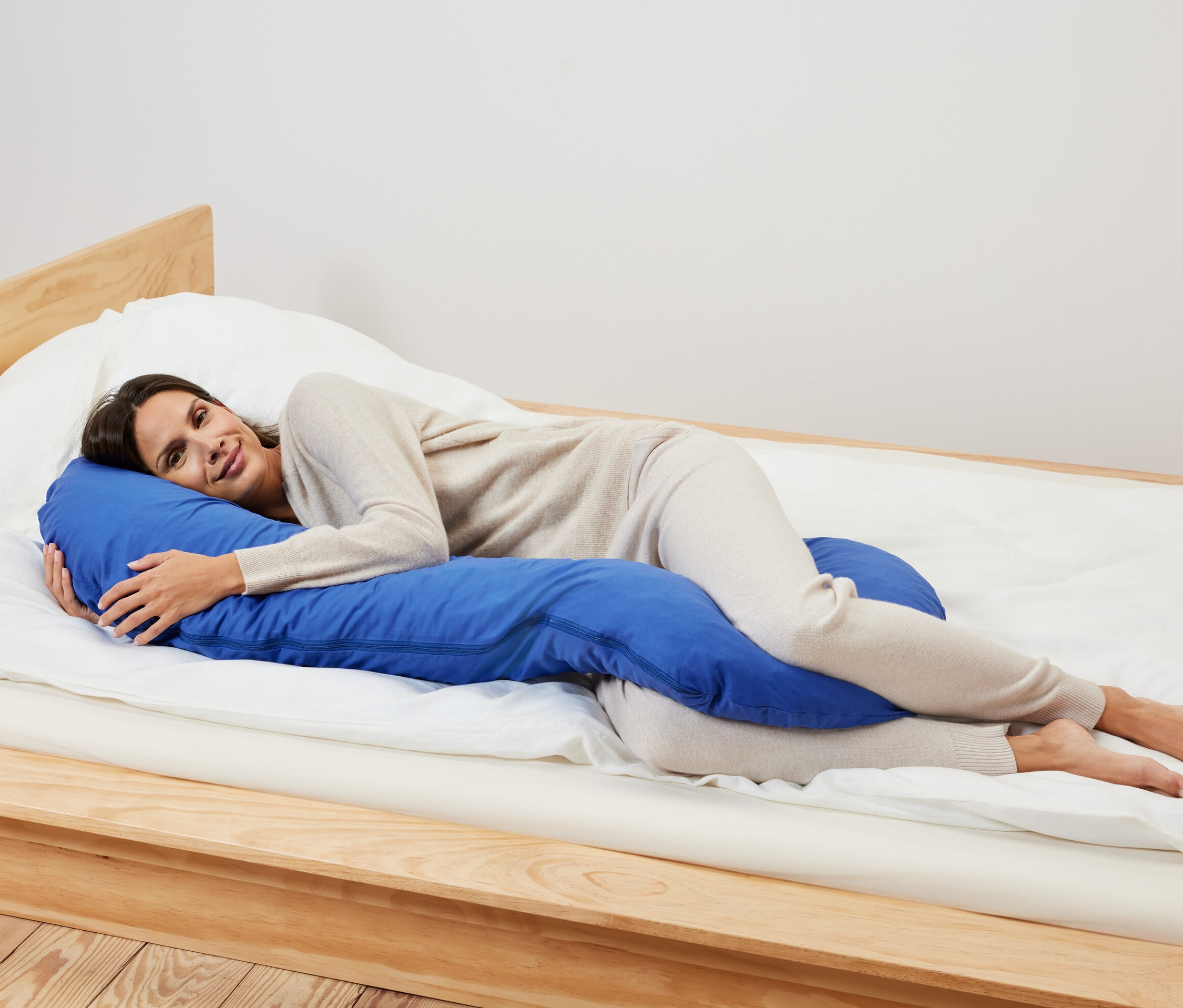 Une femme est allongée sur le côté sur un lit et serre dans ses bras un coussin XL bleu pour dormir sur le côté.