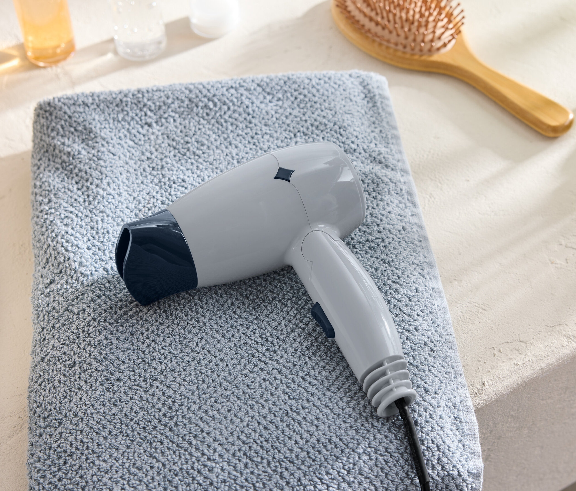 Un sèche-cheveux de voyage gris est posé sur une serviette bleue à côté d'une brosse à cheveux.