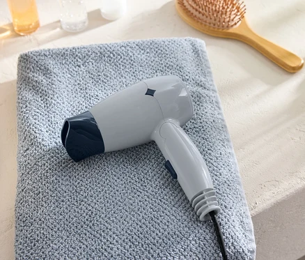 Un sèche-cheveux de voyage gris est posé sur une serviette bleue à côté d'une brosse à cheveux.