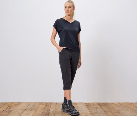 Femme posant en t-shirt technique bleu, pantacourt noir et chaussures de randonnée.