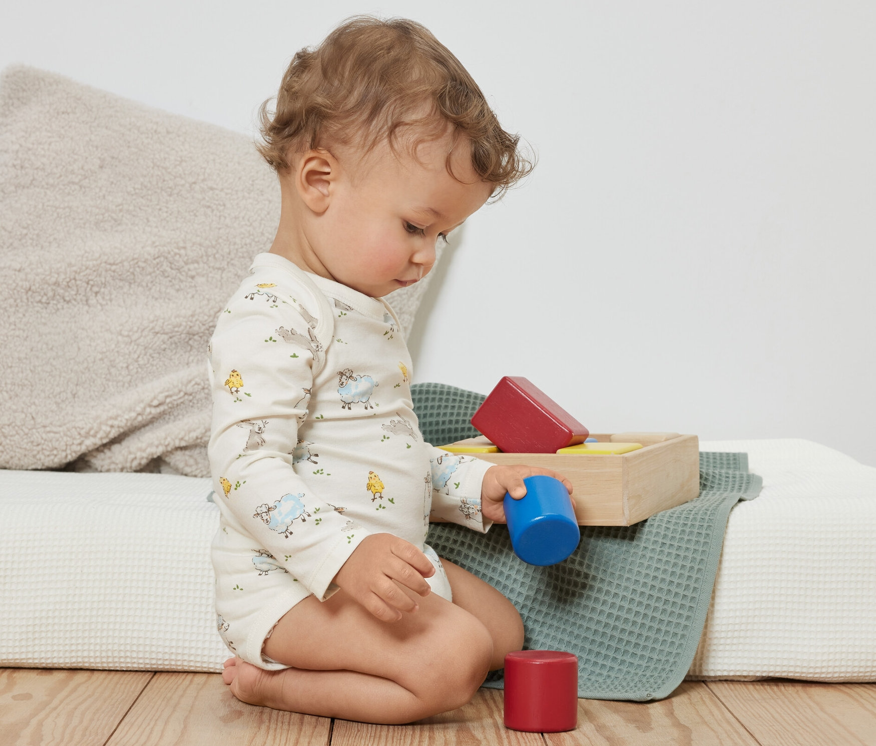 Un bambin bouclé est assis par terre et joue avec des blocs de couleur. Il porte 3 bodys pour bébé avec fonction évolutive, bleu.