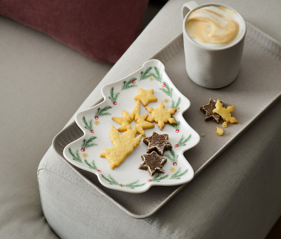 Une assiette en forme de sapin avec des biscuits et une tasse de café sur un plateau sur un canapé.