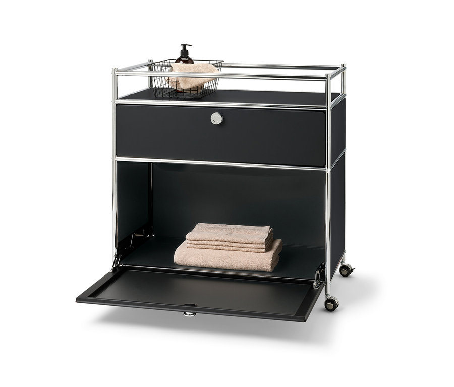 Commode métallique « CN3 » avec un tiroir, un compartiment à abattant et contour. Panier avec serviette et flacon doseur sur le dessus. Serviettes pliées dans le compartiment inférieur.
