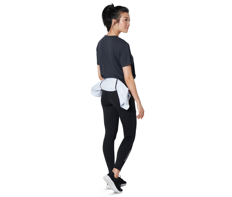 Une femme se tient de profil et porte un legging de course noir haute performance.