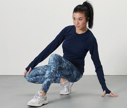 Femme en haut foncé et legging de sport, bleu foncé/menthe, posant accroupie.