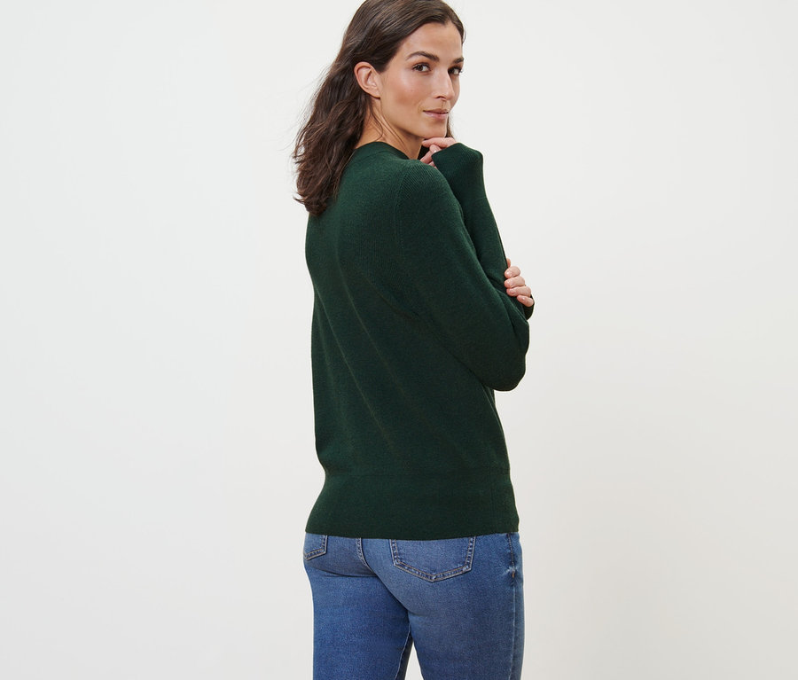 Femme posant en pull en maille fine vert et jean.