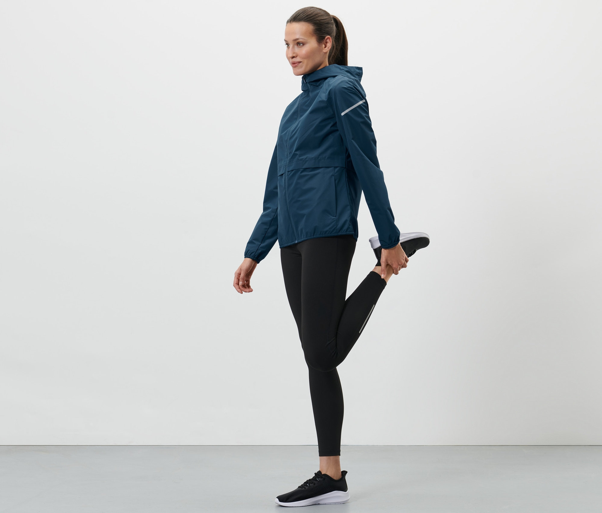 Femme étirant sa jambe et portant une veste de sport coupe-vent bleue.