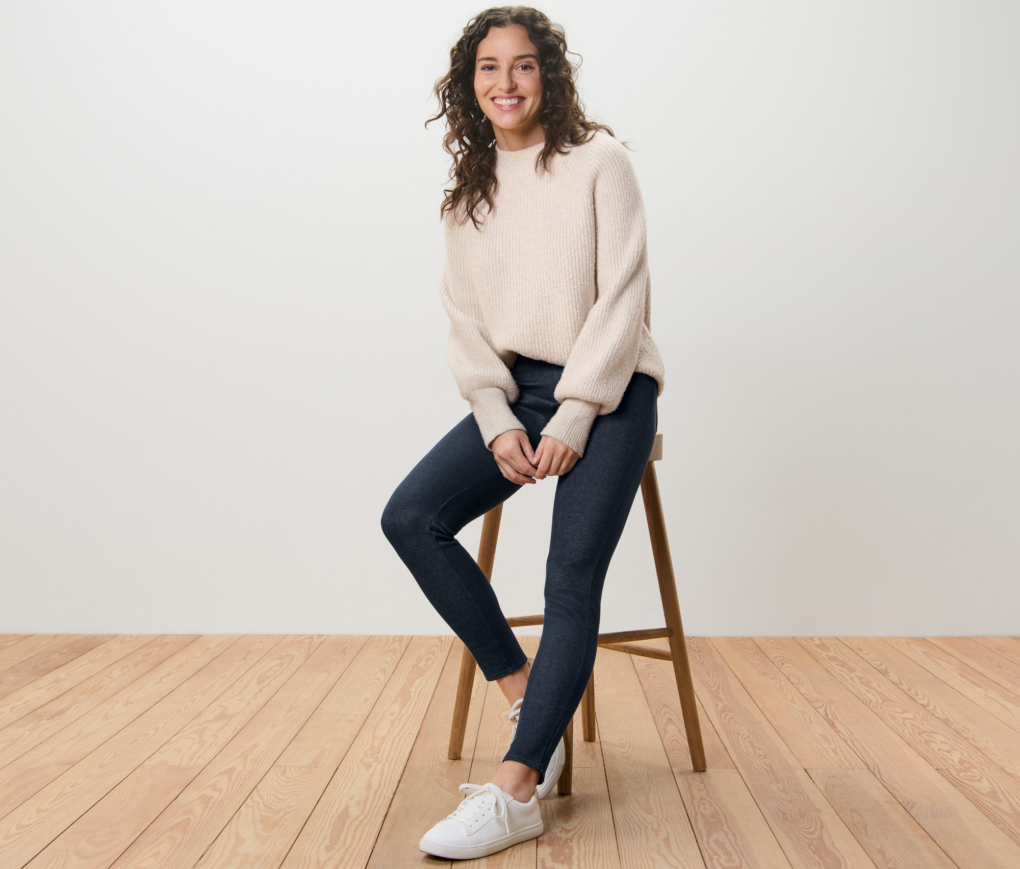 Femme assise sur un tabouret portant un legging doublé à l’aspect jean et un pull.