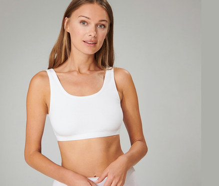 Femme aux longs cheveux bruns portant une brassière SCHIESSER blanche et des sous-vêtements blancs, regardant devant elle.