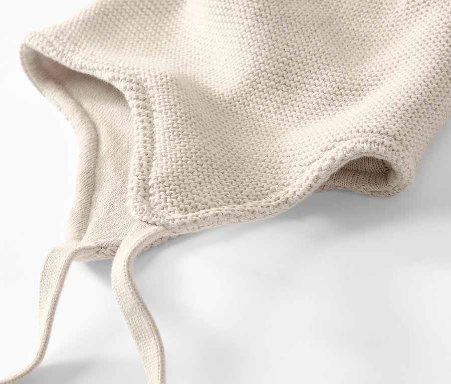 Gros plan d'un bonnet et d'une écharpe en maille pour bébé de couleur crème sur un fond blanc.