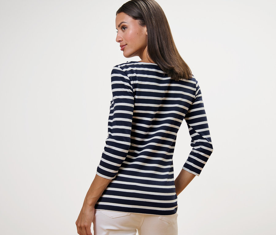 Une femme porte un t-shirt rayé manches 3/4, à rayures bleu marine, et un pantalon clair.