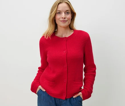 Une femme pose en cardigan rouge en maille structurée et un jean bleu.