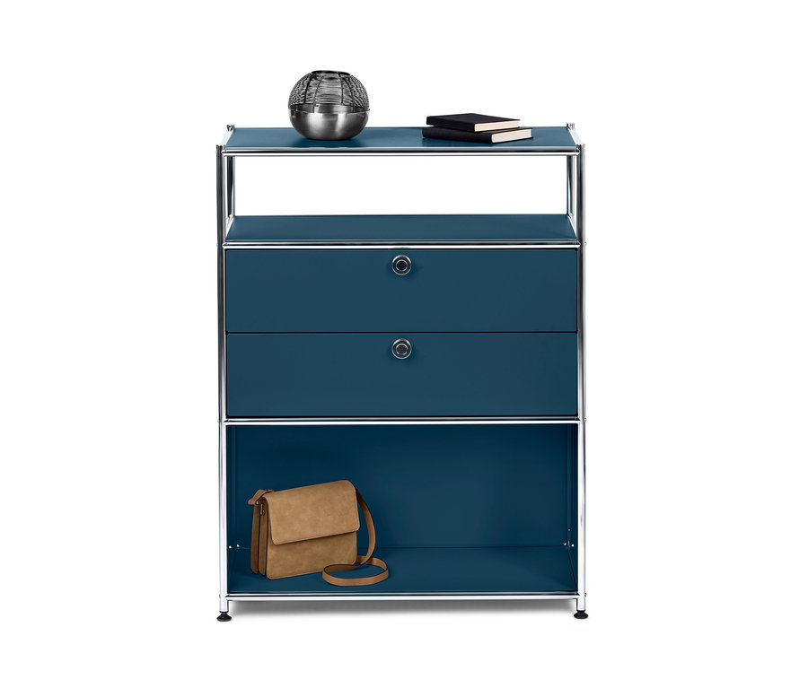 Commode bleue « CN3 » avec 2 tiroirs. Sur l'étagère supérieure se trouvent une boule décorative argentée et deux livres. Sur l'étagère inférieure se trouve un sac à main marron.