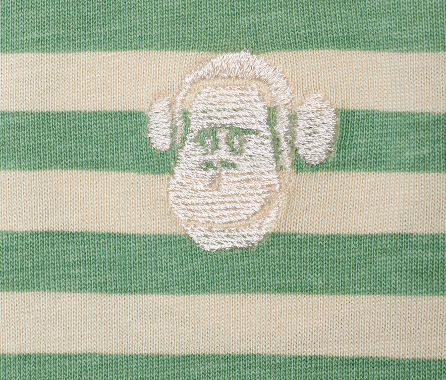 Gros plan sur 2 t-shirts pour enfant avec un motif de singe portant des écouteurs sur un fond rayé vert et blanc.