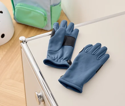 Des gants bleus reposent sur une armoire blanche, avec un sac à dos et un casque en arrière-plan.