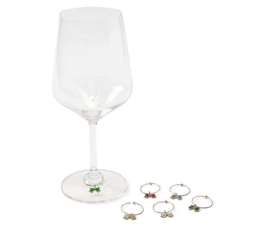 Un verre à vin vide avec un papillon vert sur le pied et cinq autres papillons de couleurs rouge, or, bleu et vert à côté.