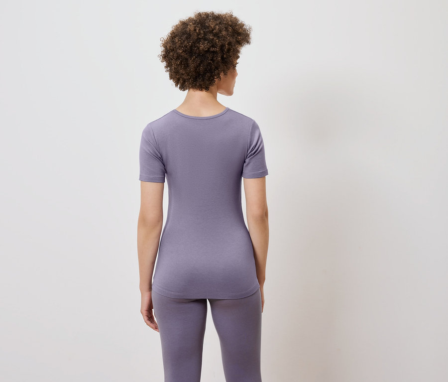 Vue de dos, une femme aux cheveux bouclés portant un t-shirt violet et un legging.