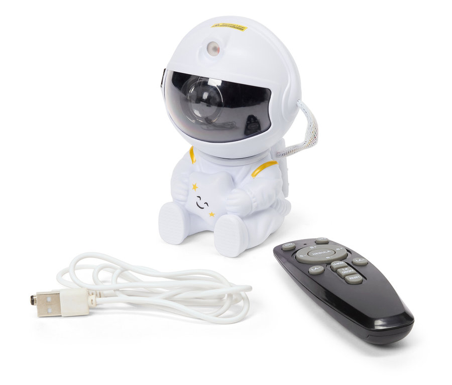 Un projecteur de ciel nocturne blanc en forme d'astronaute est assis à côté d'une télécommande noire et d'un câble USB blanc.