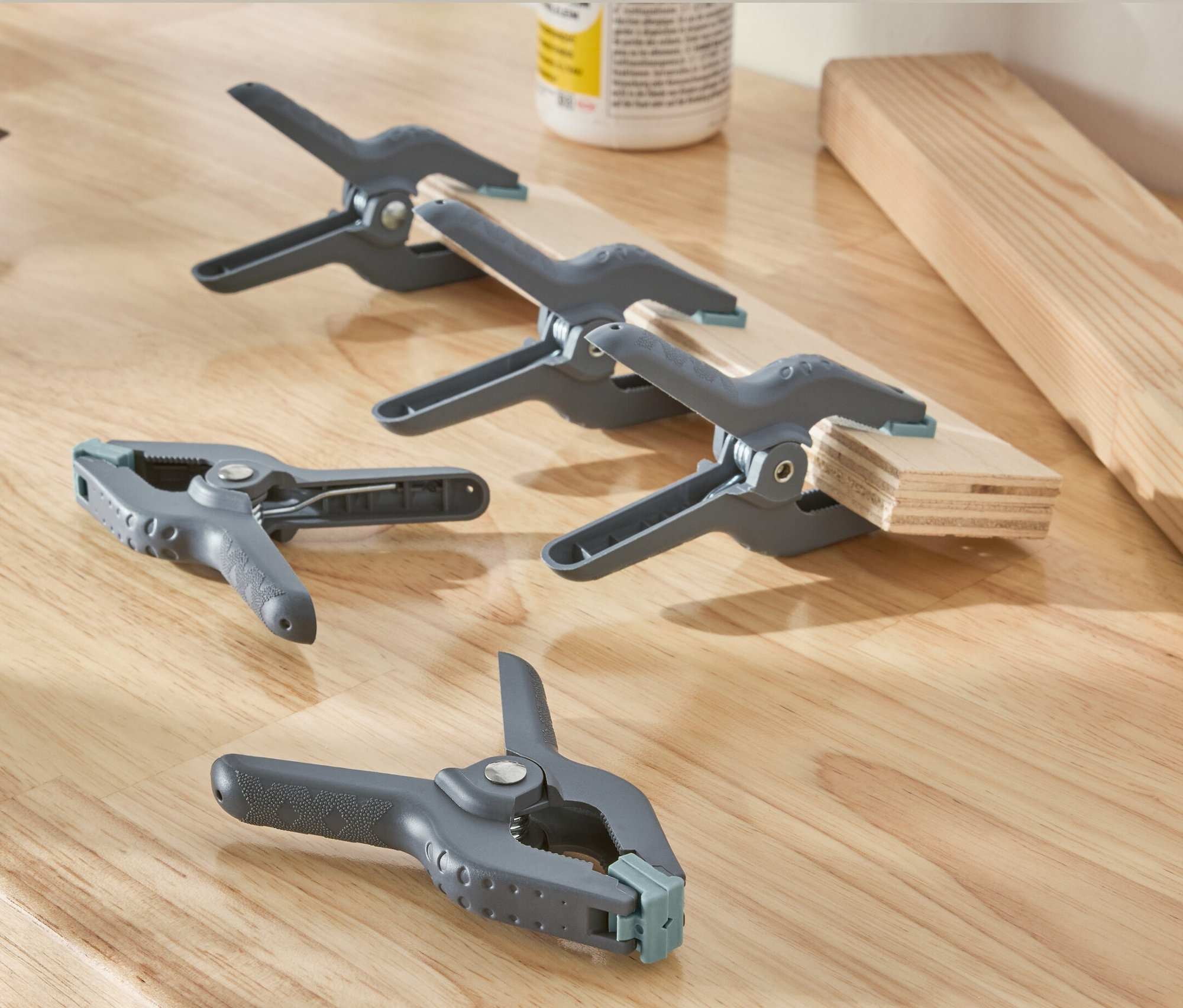 Sur une surface en bois reposent une perceuse et cinq serre-joints à ressort gris.