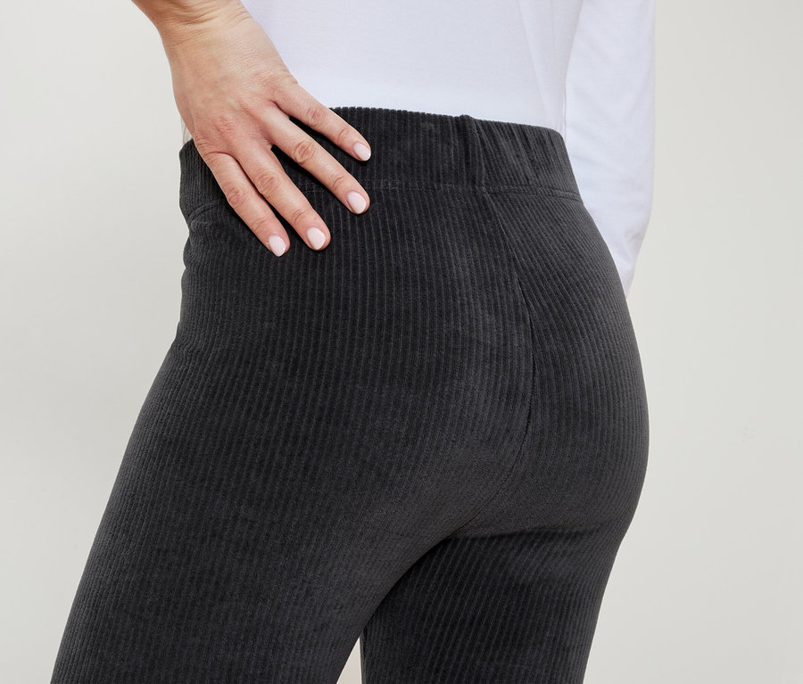 Une femme en pantalon côtelé gris pose sa main sur sa hanche.