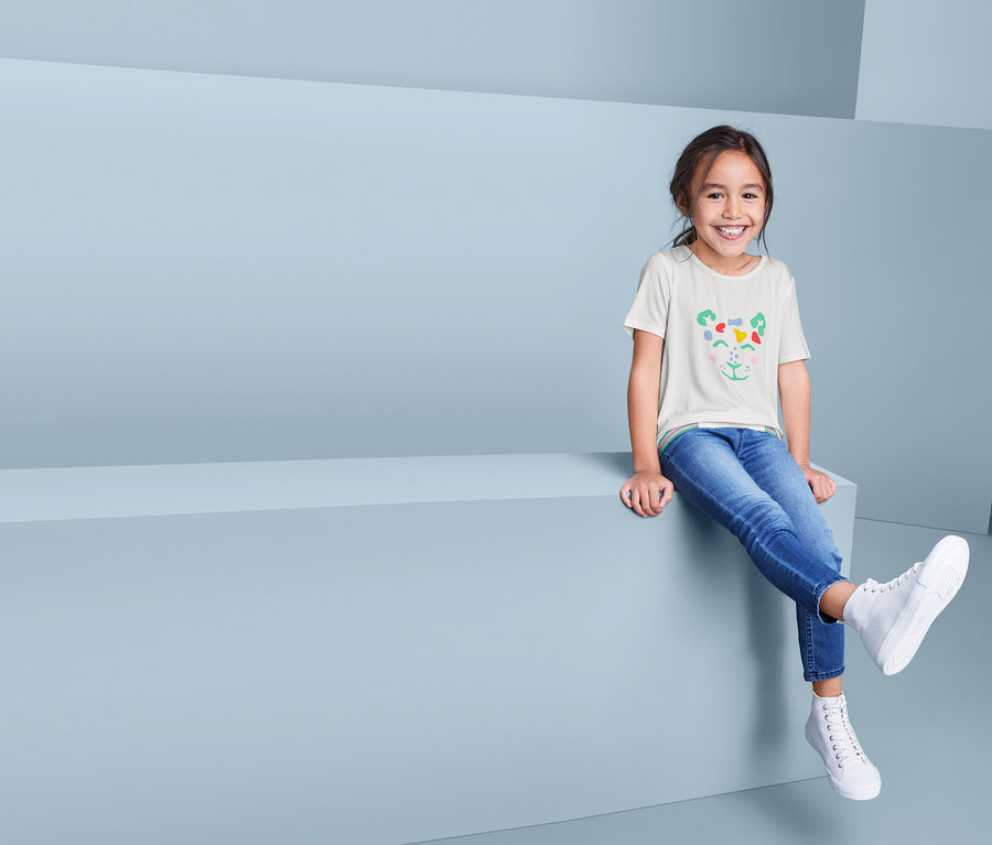 Une fille souriante est assise et porte un t-shirt à enfiler, un jean et des chaussures.