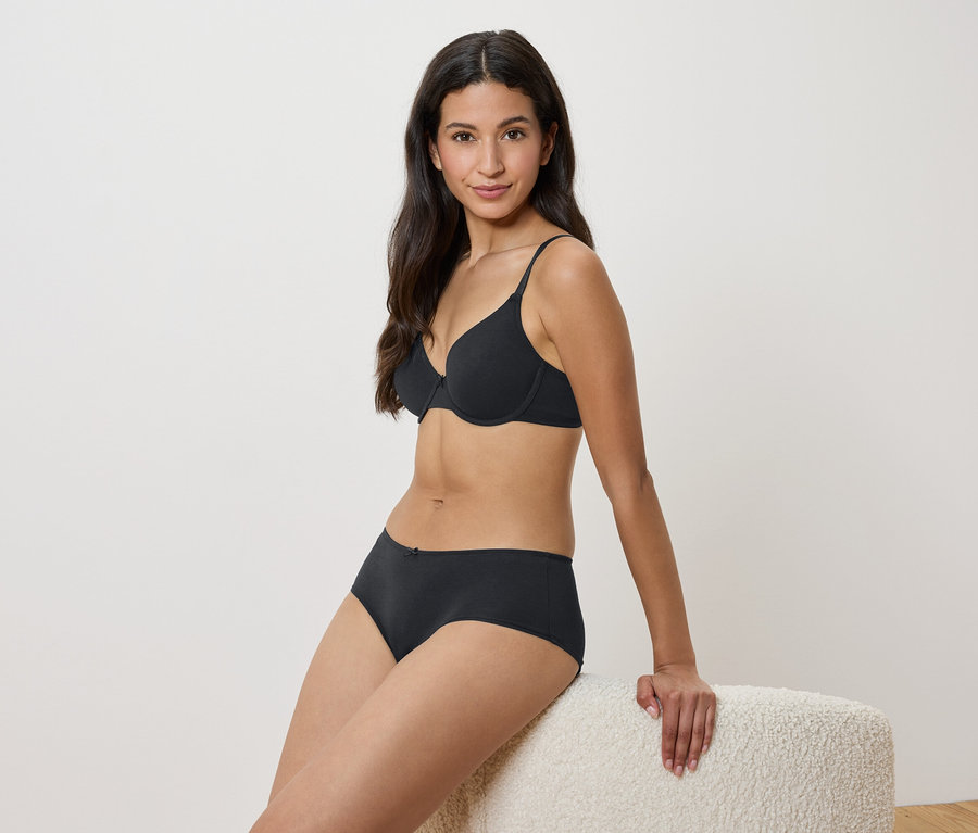 Femme assise sur un tabouret en soutien-gorge et culotte noirs.