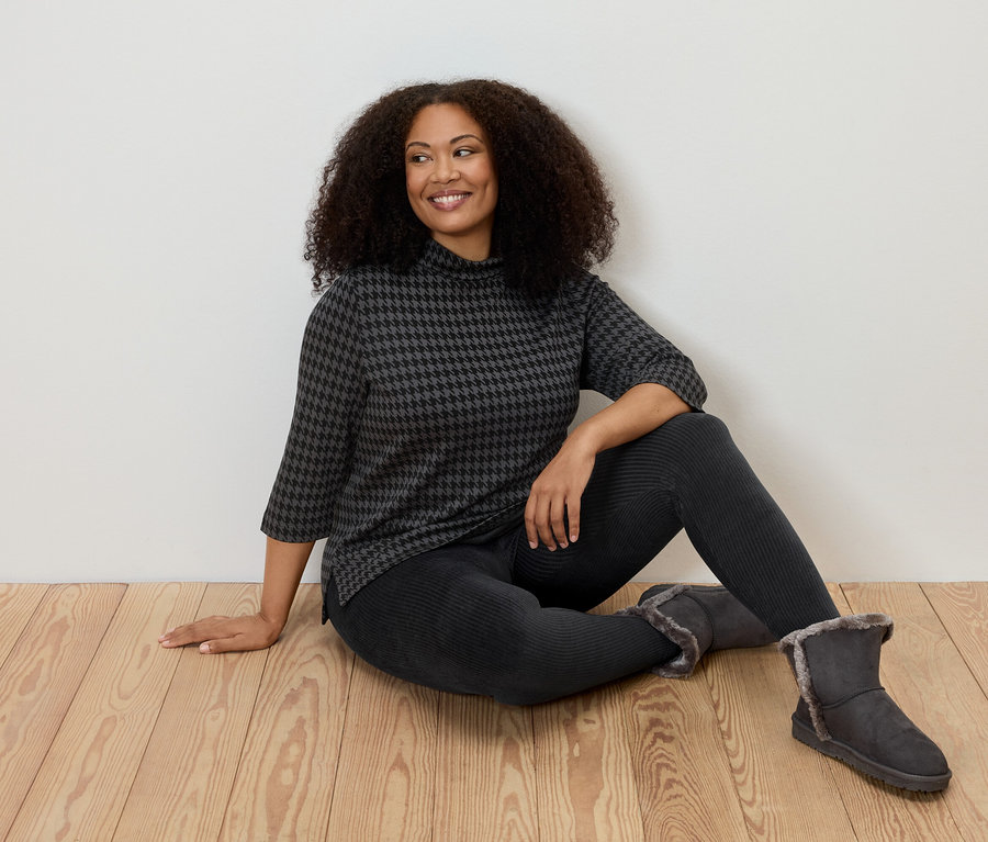 Femme assise par terre portant un legging en velours côtelé, un haut à motifs et des bottes.