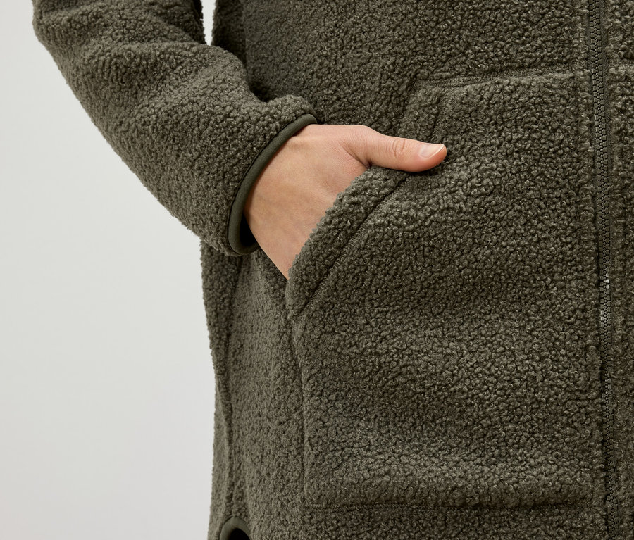 Main dans la poche d'une veste en polaire teddy vert olive.