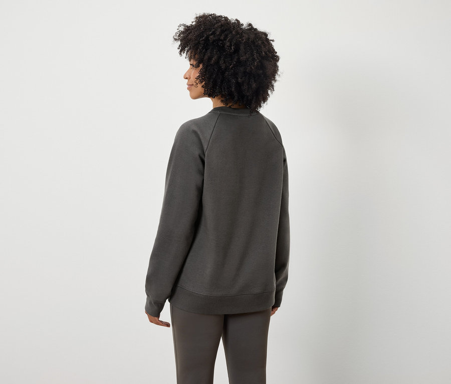 Vue arrière d'une femme avec une coiffure afro portant un sweat-shirt et un pantalon gris.