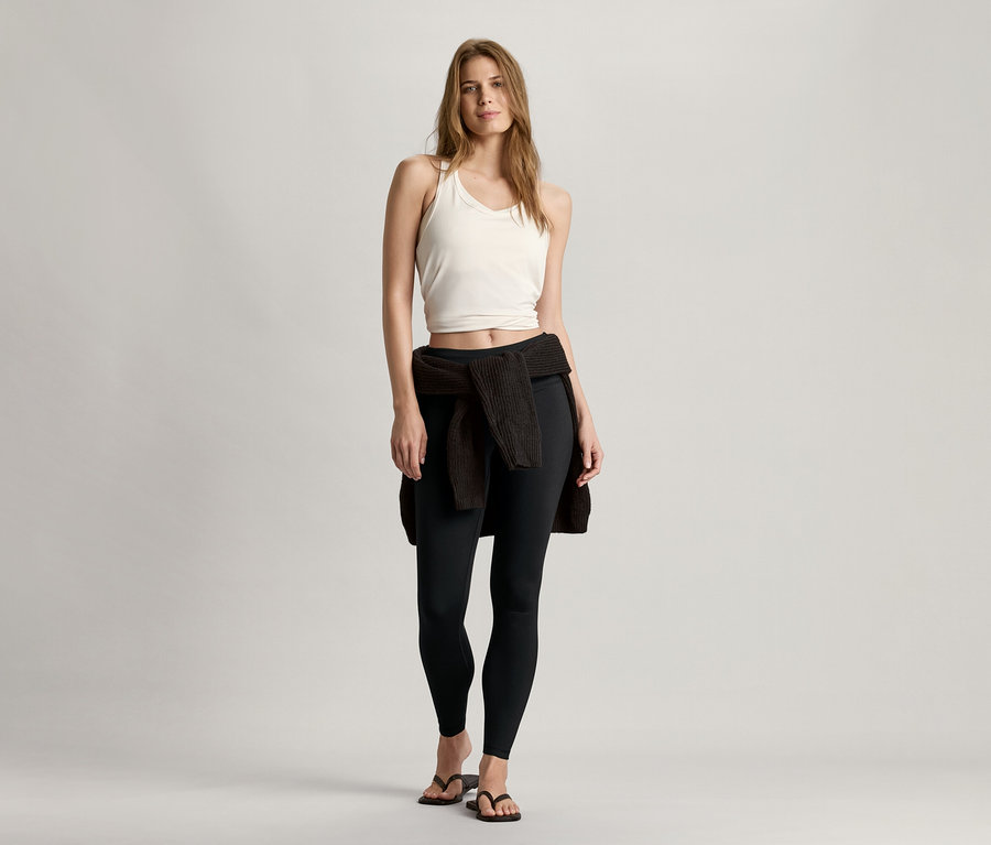 Femme debout portant un bustier de sport Seamless blanc, un legging noir et un cardigan noué autour de la taille.